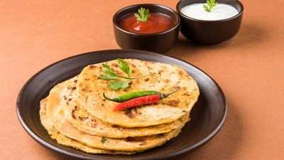 Stack of buttery stuffed potato parathas with yogurt and ketchup.