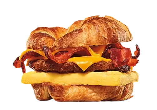 A breakfast sandwich layered with a sausage patty, bacon strips, egg, and melted cheese inside a croissant.