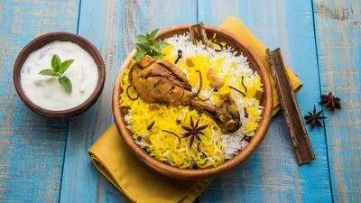 A bowl of layered chicken biryani with raita on a blue wooden table.