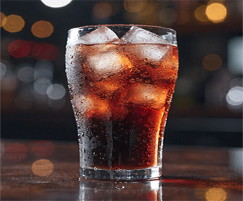 Glass of dark cola with ice cubes and blurred night lights.