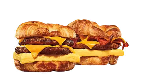 Two loaded breakfast croissant sandwiches with sausage and bacon.