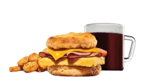 A warm breakfast biscuit sandwich layered with ham, egg, and cheese, paired with hashbrowns and black coffee.