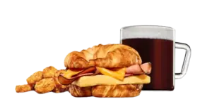 A flaky croissant breakfast sandwich with savory ham, egg, and cheese, served with hashbrowns and hot coffee.