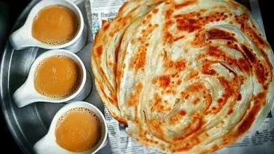 A large, crispy layered lachha paratha served on a metal tray alongside