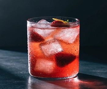 Red bubbly drink in a glass with large ice cubes and whole strawberries.