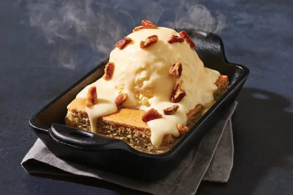 Steaming hot cake in a cast iron skillet topped with melting ice cream and pecans.